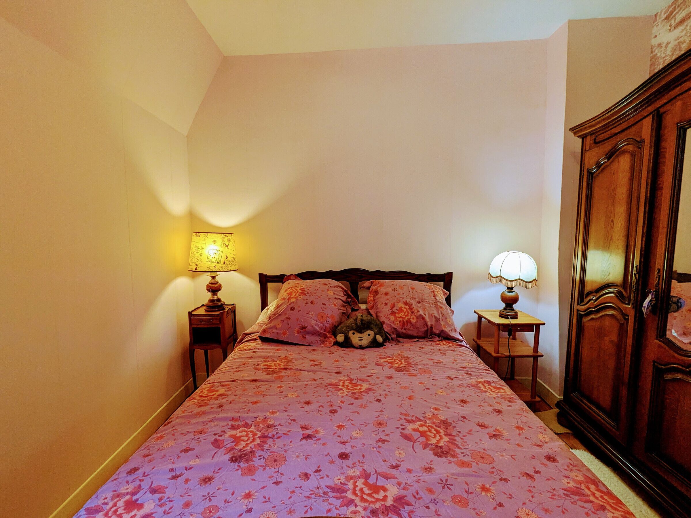 Een slaapkamer met een bed, twee nachtkastjes, een houten garderobe en twee wandlampen.