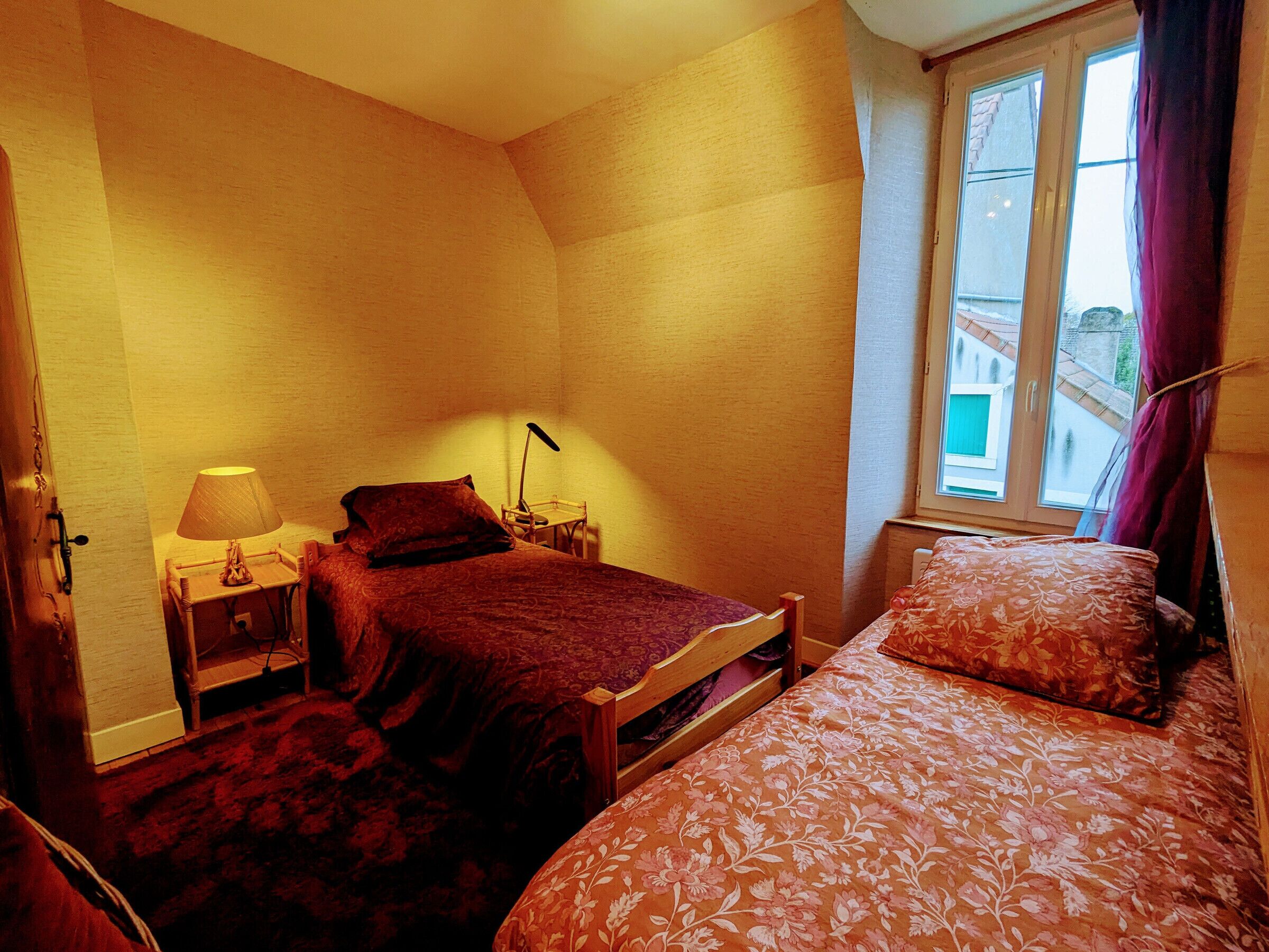 A bedroom with two beds, a nightstand, a lamp, and a window with curtains.