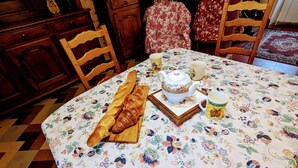 A dining table with a floral tablecloth, a loaf of bread, a teapot, and two cups. - Cozy Cottage in Quiet Village with Nearby River- Access, Terrace, & Private Parking (Le Menoux)