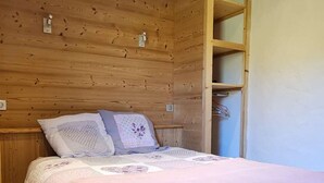 A wooden cabin bedroom with a bed, pillows, and a shelf unit. - Renovated Apartment in La Turche, Les Gets - 1BR, Sleeps 4, Balcony, Parking, Ski Storage (Les Gets)