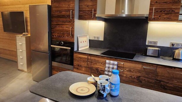 A modern kitchen with wooden cabinetry, stainless steel appliances, and a flat-screen TV mounted on the wall. - Renovated Apartment in La Turche, Les Gets - 1BR, Sleeps 4, Balcony, Parking, Ski Storage (Les Gets)