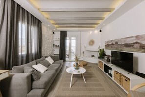 A modern living room with a grey sofa, a round coffee table, a flat-screen TV, and a stone accent wall.