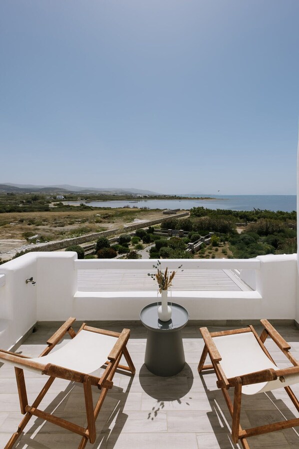 A terrace with a view of the sea, a table with a vase, and two wooden chairs.