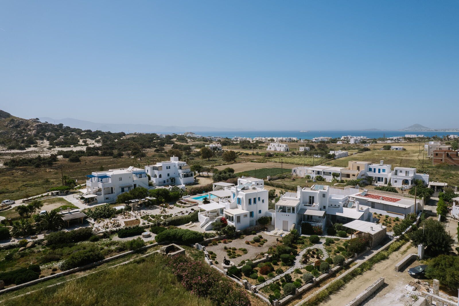 A coastal residential area with white buildings, a swimming pool, and a view of the sea.