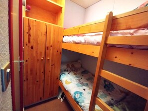 Ein Etagenbett mit unterem Bett, ein zweitüriger Holzschrank und ein kleines Regal über dem Bett.