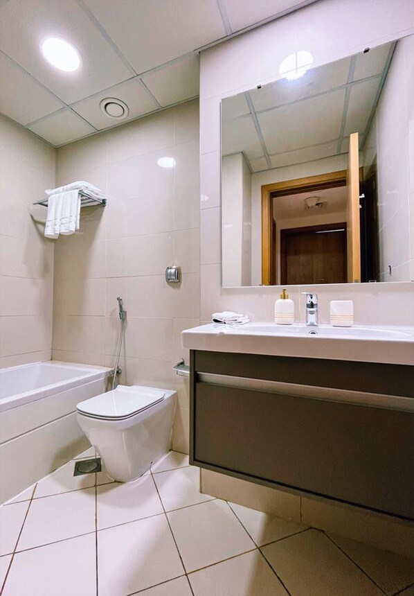 A bathroom with a bathtub, toilet, and a large mirror above the sink.