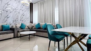 A modern living room with a sectional sofa, a dining table with chairs, and a marble wall. - Lux High Rise Marina Apartment (Dubai)
