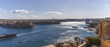 Paisagem costeira com um porto, navios e um edifício histórico imponente.