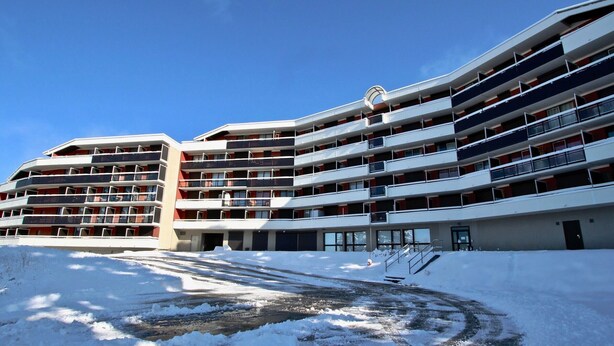 Un hotel de varios pisos con fachada curva, balcones en cada planta y suelo cubierto de nieve.