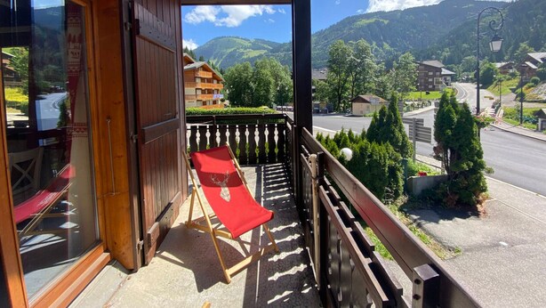 Ein Holzbalkon mit einem roten Stuhl, einem Holzzaun und Blick auf Berg und Stadt.