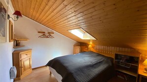 Ein Schlafzimmer mit schrägen Wänden, einem Bett, einem kleinen Schreibtisch mit Lampe und einem Kleiderschrank.