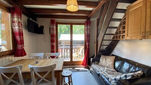 Ein gemütliches Zimmer mit einem Holzesstisch, weißen Stühlen, einem schwarzen Ledersofa und einer Treppe.