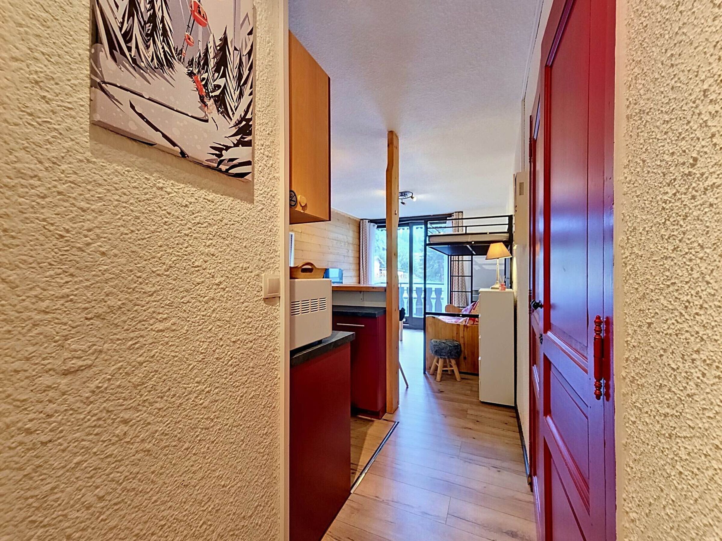 A narrow hallway with a kitchen area, a dining space, and a red door.