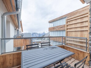 Un balcón con mesa y sillas, paneles de madera y vistas a las montañas.