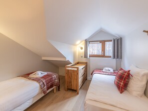 Une petite chambre accueillante, avec deux lits, un berceau en bois et une fenêtre avec des rideaux.