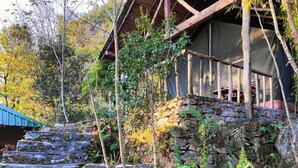 Un escalier en pierre rustique mène à un chalet en bois doté d’un toit de chaume, le tout étant entouré d’une végétation luxuriante et d’arbres.