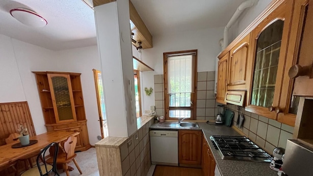 A compact kitchen with wooden cabinets, a gas stove, a dishwasher, and a window providing natural light.