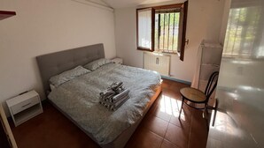 A bedroom with a bed, a nightstand, a chair, a window, and a radiator.