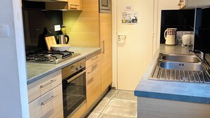 A compact kitchen with wooden cabinets, a built-in oven, a microwave, and a stainless steel sink.