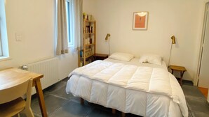 A bedroom with a bed, a desk, a bookshelf, and a radiator.