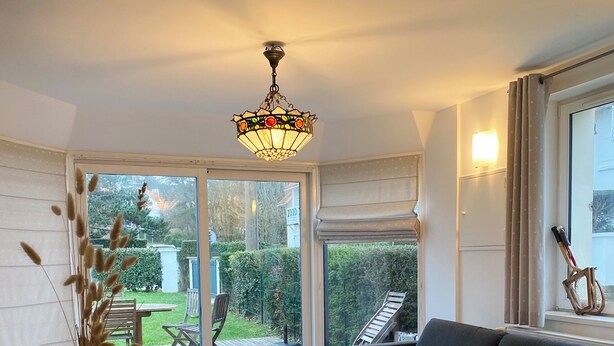 A modern living room with a dining table, sofa, and a large window with a view of the garden.