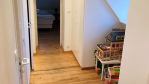 A narrow hallway with wooden flooring leading to a bedroom with a bed and nightstand.