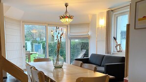 A dining area with a wooden table and chairs, a vase with dried plants, and a chandelier.