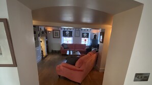 Een gang die uitkomt in een woonkamer met een roze bank en een eethoek met een tafel en stoelen.