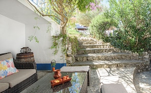 A stone staircase leading up to a building, a wicker sofa with cushions, a table with a basket of apples, and a potted plant. - Quinta de São Pedro (Almada)