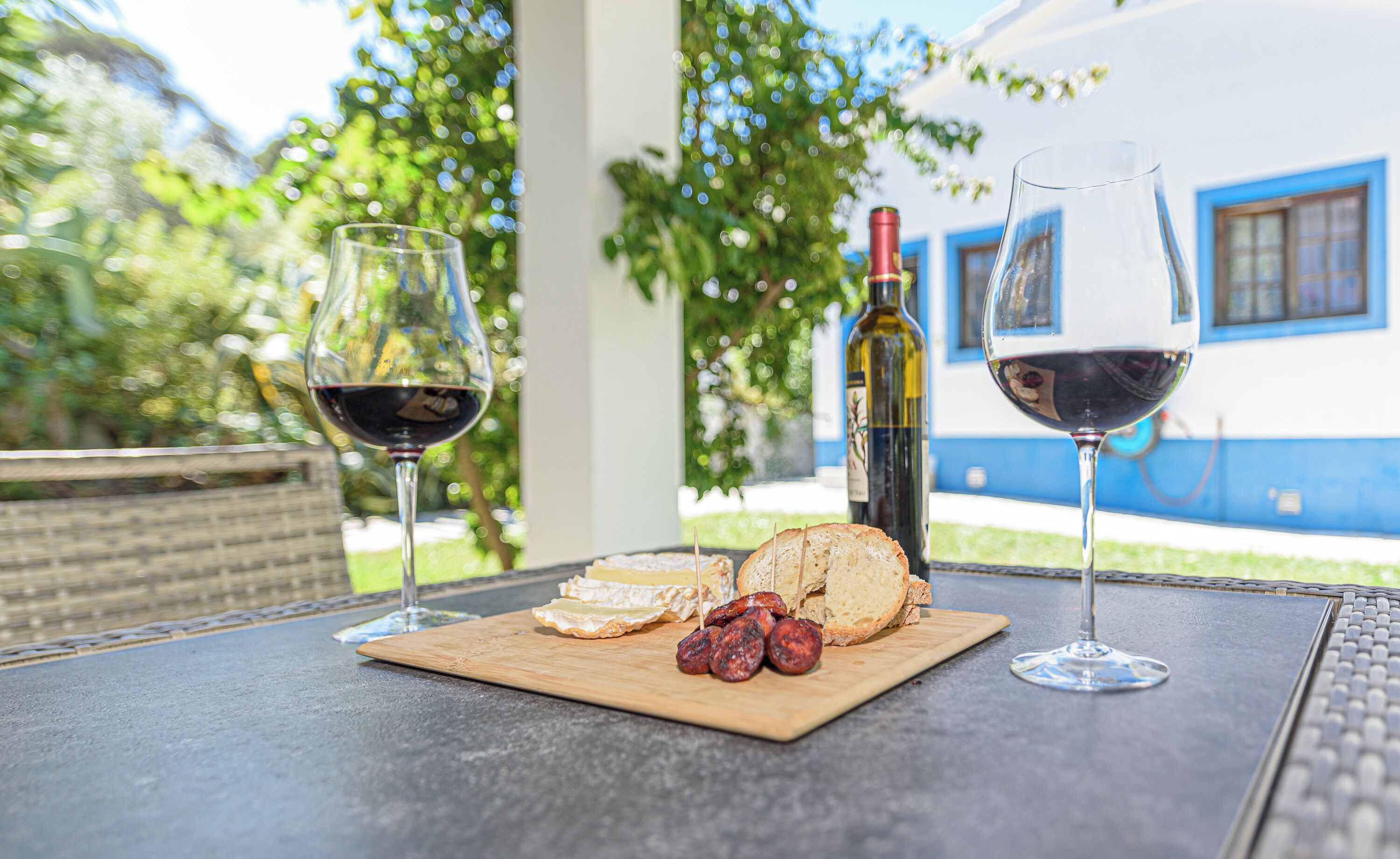 A table with two wine glasses, a bottle of wine, and a wooden board with bread and sausage slices.