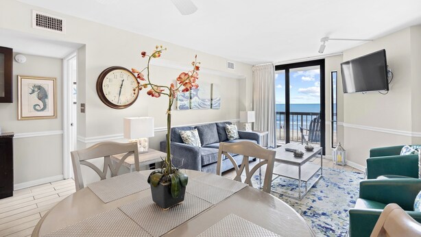 A modern living room with a dining area, a large clock, and a view of the ocean.
