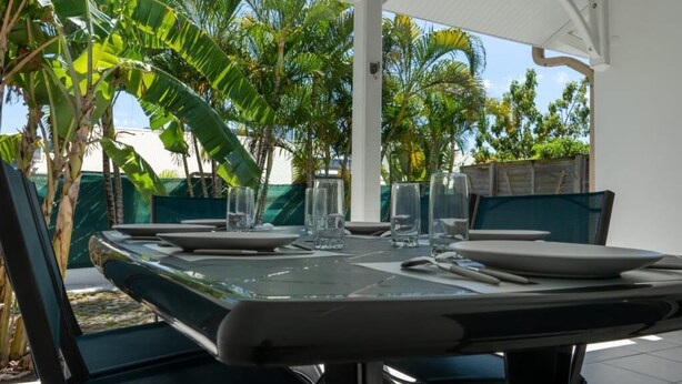 An outdoor dining area with a table set for two, surrounded by lush tropical plants.