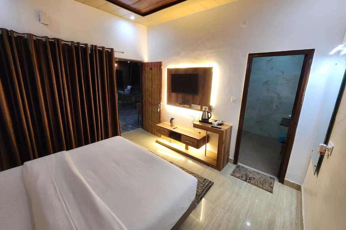 Ein Hotelzimmer mit einem Bett, einem Nachttisch mit Lampe, einem an der Wand befestigten Fernseher und einer Tür zu einem Balkon.