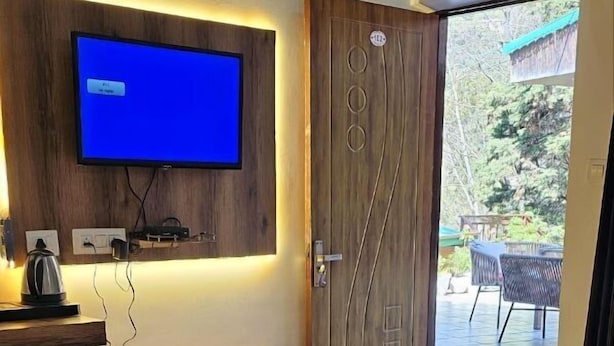 Un dormitorio moderno con una cama grande, un televisor de pantalla plana montado en un panel de madera, un escritorio con un hervidor y una puerta que da a un patio exterior.