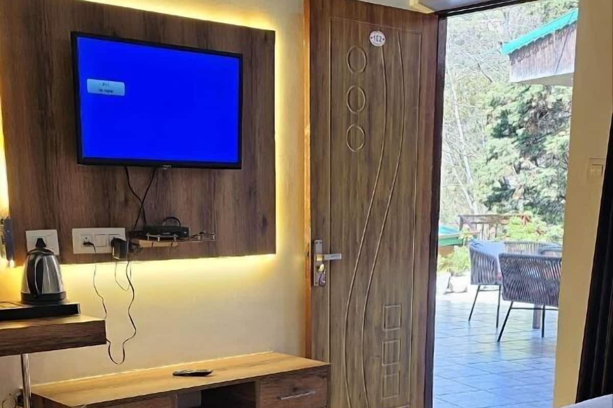 Ein modernes Schlafzimmer mit einem großen Bett, einem Flachbildfernseher an einer Holzverkleidung, einem Schreibtisch mit Wasserkocher und einer Tür zu einem Außen-Terrassenbereich.