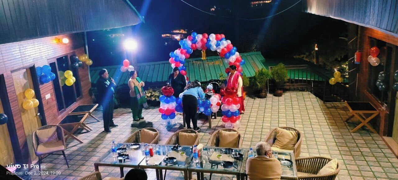 An outdoor dining area with tables and chairs, a tiled floor, and a decorative arch made of balloons.