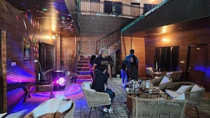 Un espacio interior amplio con mobiliario de mimbre, una escalera y una cabina de DJ.
