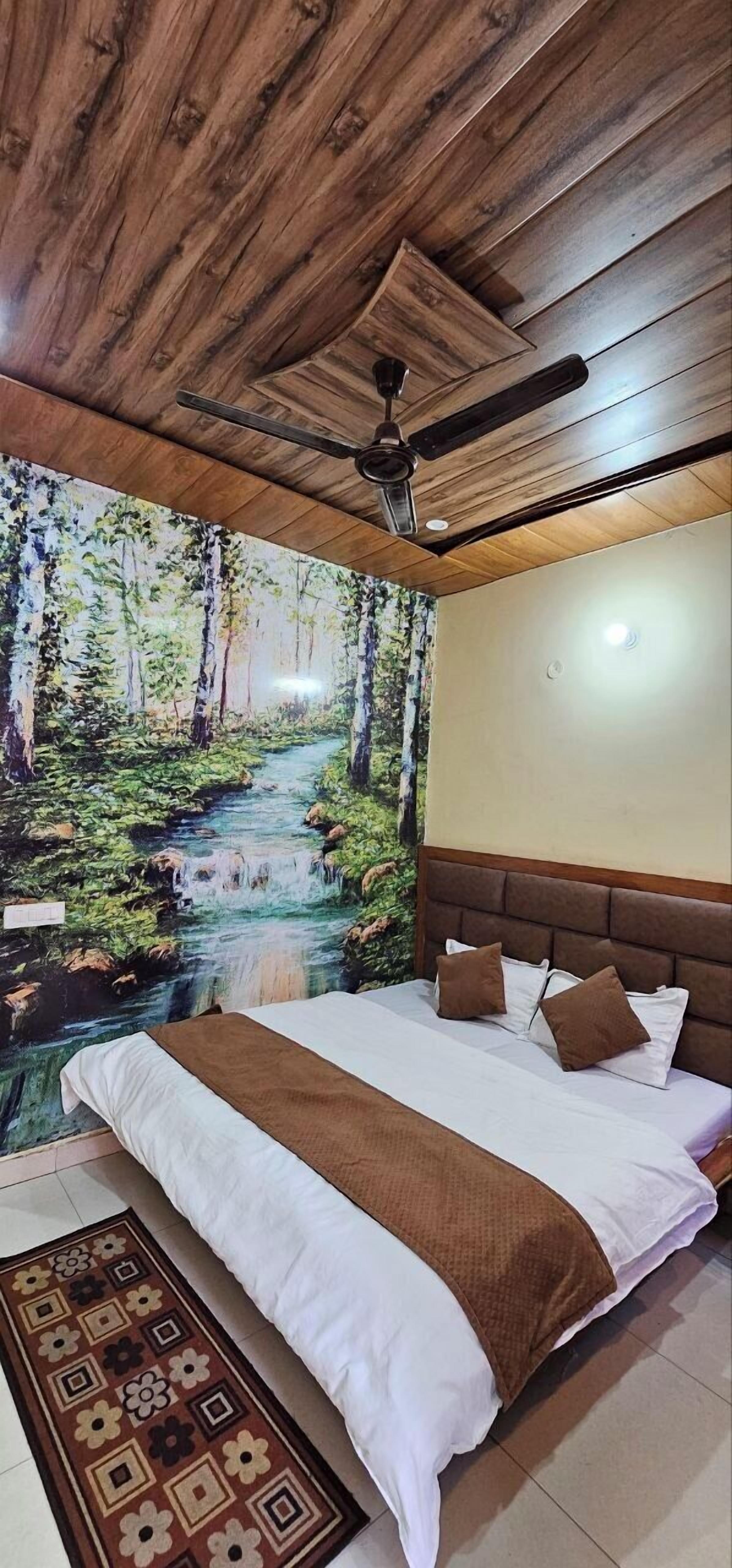 A bedroom with a wooden ceiling, a ceiling fan, a bed with white bedding and brown pillows, and a forest-themed wall mural.