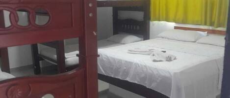 A dormitory room with bunk beds, a bed, a window with yellow curtains, and a white wall.