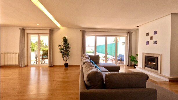 A spacious living room with a large sofa, a fireplace, and a sliding glass door leading to an outdoor area. - Beloura (Sintra)