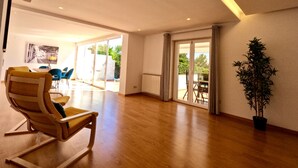 A spacious living area with a wooden floor, a large sliding glass door leading to an outdoor patio, and a potted plant. - Beloura (Sintra)