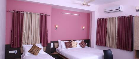 A hotel room with two beds, a ceiling fan, an air conditioning unit, and a desk with a chair.