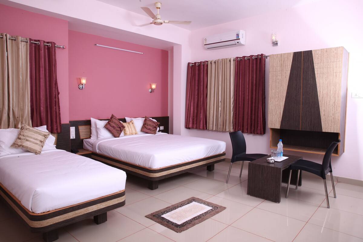 A hotel room with two beds, a desk, a chair, an air conditioner, and a ceiling fan.
