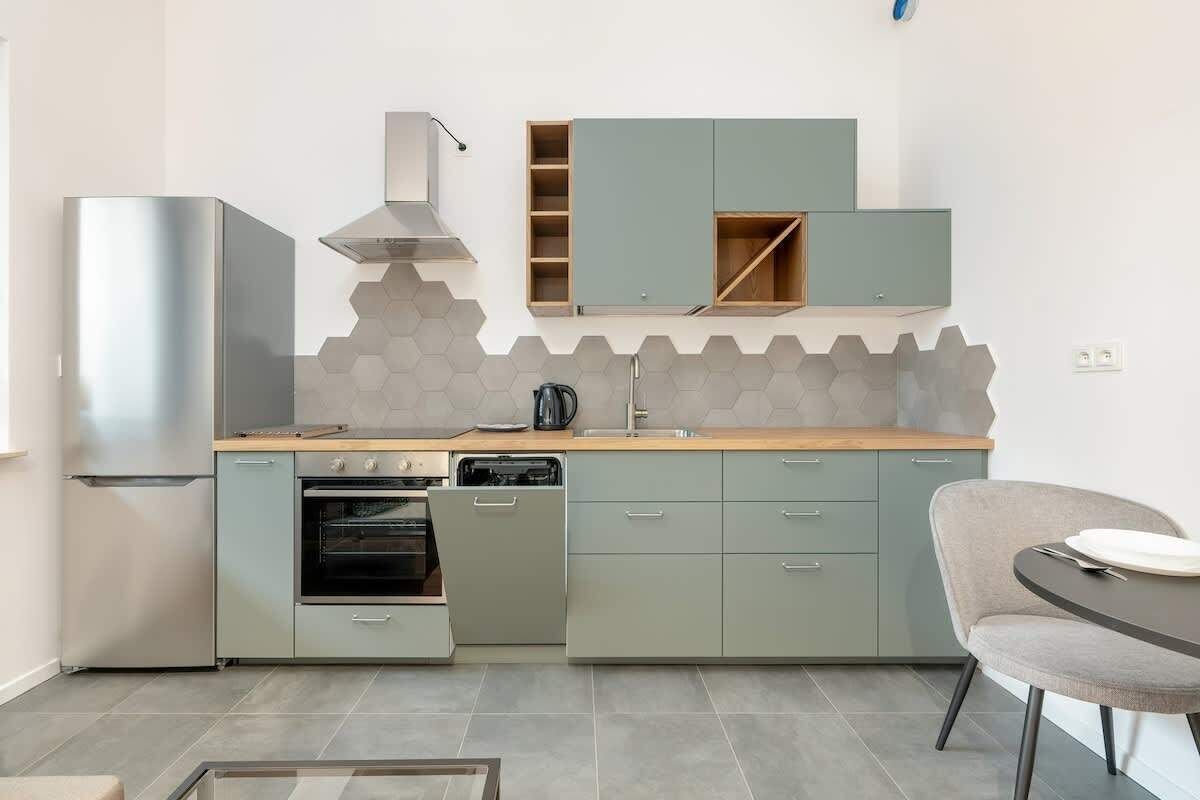 Een moderne keuken met grijze kastjes, een roestvrijstalen afzuigkap en een achterwand van honingraatmozaïek.