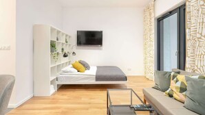 Ein modernes Schlafzimmer mit einem Bett, einem Fernseher, einer Couch und einem weißen Regal.