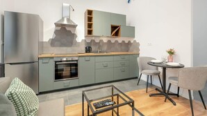 Eine moderne Küche mit Einbauofen, Edelstahl-Kühlschrank und Essbereich mit rundem Tisch und zwei Stühlen.