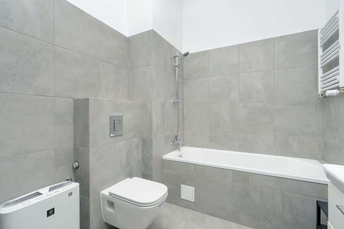 Un baño moderno con azulejos grises, un inodoro blanco, una bañera blanca y un perchero para toallas.
