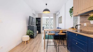 Una cocina moderna con armarios de madera, un comedor con taburetes y un amplio ventanal con vistas a edificios.