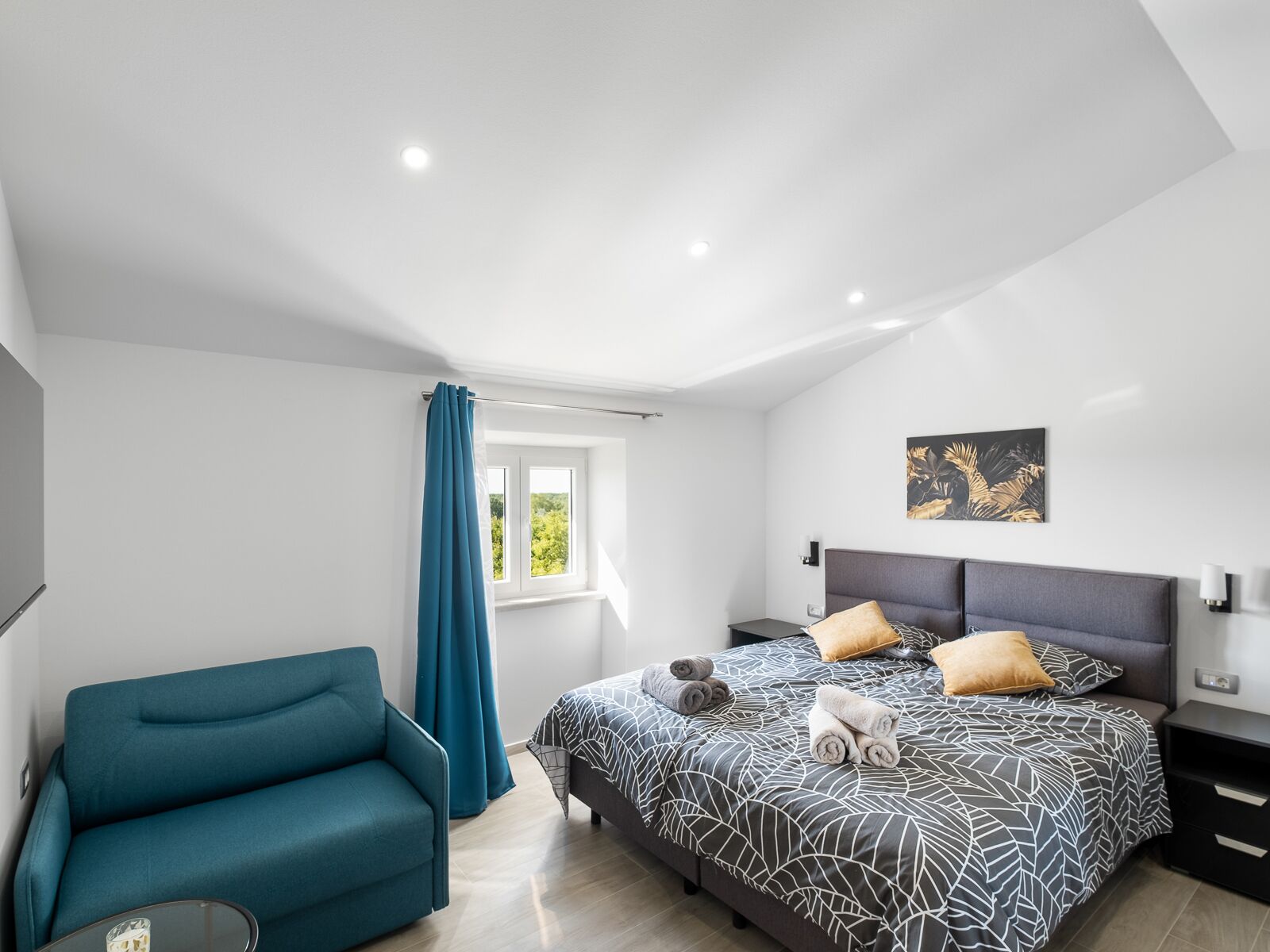 A modern bedroom with a bed, a sofa, a window with curtains, and a painting on the wall.