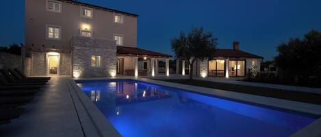 A modern house with a swimming pool, stone exterior, and multiple illuminated windows.